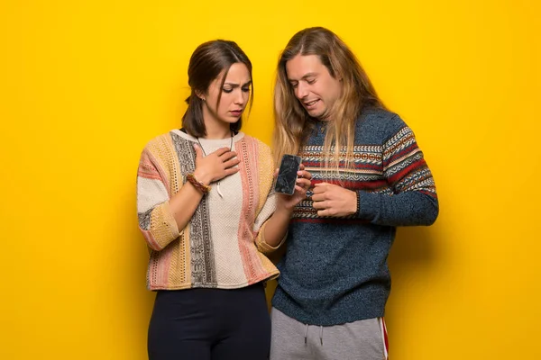 Hippie Casal Sobre Fundo Amarelo Com Conturbado Segurando Smartphone Quebrado — Fotografia de Stock