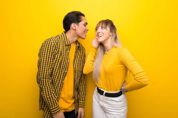 耳に手を置くことによって何かを聞いて鮮やかな黄色の背景の上に若いカップル — ストック写真