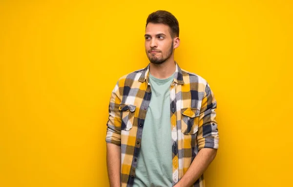 Handsome man over yellow wall with confuse face expression while bites lip