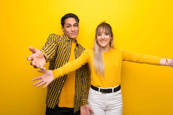 Junges Paar Vor Lebendigem Gelben Hintergrund Präsentiert Und Lädt Ein — Stockfoto