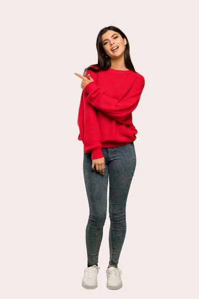 孤立した背景に製品を提示する側を指している赤いセーターとティーンエイ ジャーの女の子のフルレングス ショット — ストック写真