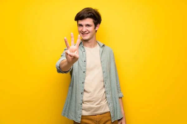 Mężczyzna Nastolatek Żółty Ścianę Trzy Szczęśliwe Liczenia Palcami — Zdjęcie stockowe