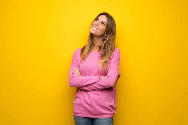 笑顔ながら見上げる黄色の壁にピンクのセーターの女性 — ストック写真