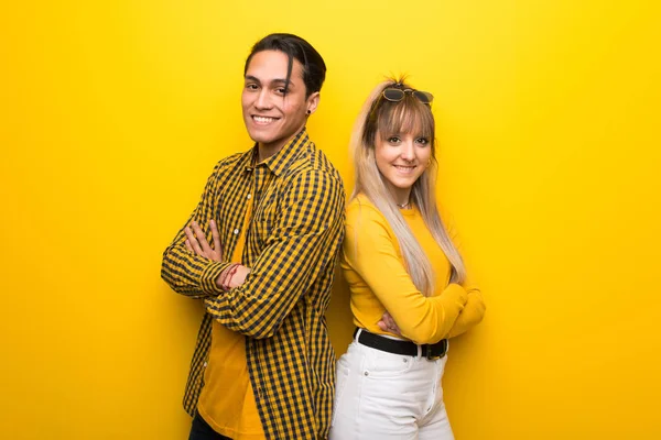 Canlı sarı arka plan üzerinde genç çift gülümseyerek kollarını yanal pozisyonda geçti tutmak