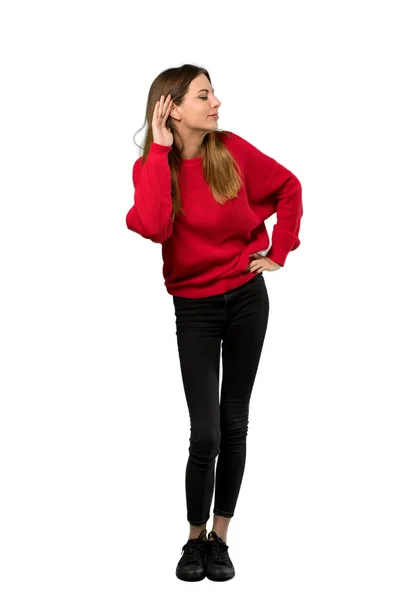 一个穿着红色毛衣的年轻女人用手放在孤立的白色背景上的耳朵来听东西的全长照片 — 图库照片