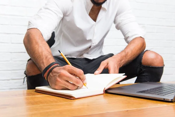 Arabic young man with laptop writing in a notebook