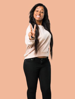 Gülümseyen ve zafer işareti izole kahverengi arka plan üzerinde gösterilen genç afro Amerikalı kadın