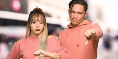 Şehirde olumsuz ifade ile başparmak aşağı işareti gösteren genç çift