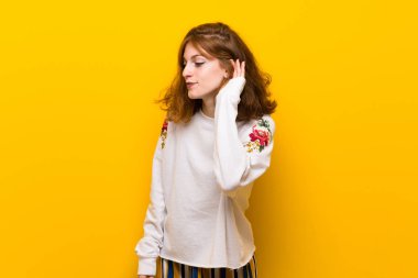 Sarı duvar için bir şey kulak el koyarak dinleme genç Kızıl saçlı kadın