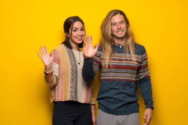 Hippi çift elle mutlu ifade ile selamlayan sarı arka plan üzerinde