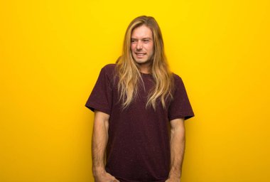 Biraz gergin ve korkmuş diş basarak sarı duvarın üzerinden uzun saçlı sarışın adam