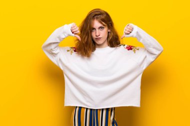 Başparmak aşağı her iki el ile gösterilen sarı duvar genç Kızıl saçlı kadın