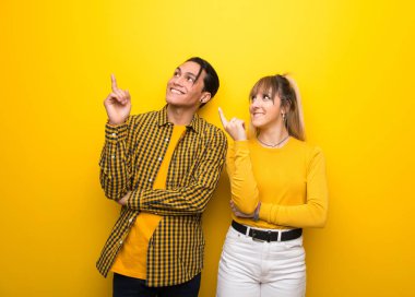 Canlı sarı arka plan üzerinde genç çift harika bir fikir işaret ve yukarı bakıyor