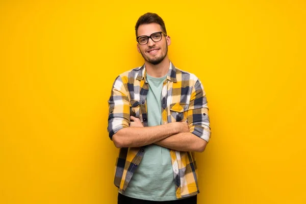 Handsome man over yellow wall with glasses and happy