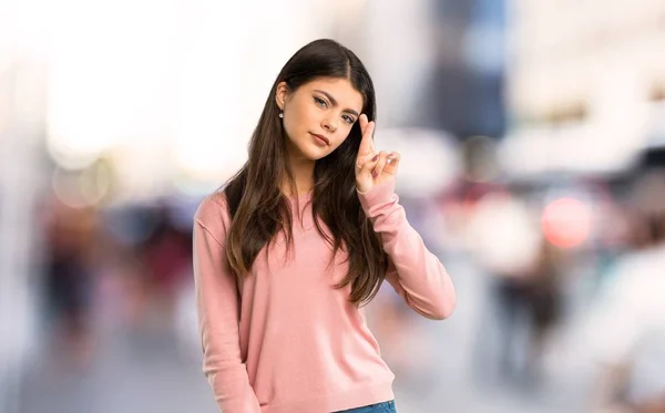 Teenager girl with pink shirt with fingers crossing and wishing the best at city