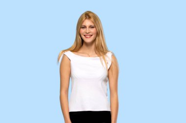 Poz ve önüne izole mavi arka plan üzerinde seyir gülüyor sarışın genç kadın
