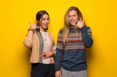 Hippi çift telefon jest yaparak sarı arka plan üzerinde. Bana arka işareti de