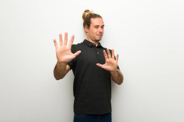 Beyaz duvar üzerinde uzun saçlı sarışın adam biraz gergin ve korkmuş elinde cepheye germe