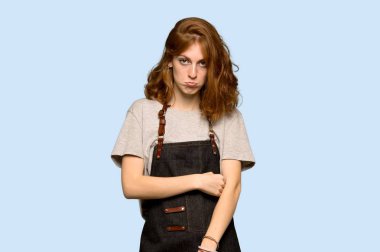 Önlük ile mavi arka plan üzerinde üzgün ve depresyonda ifade ile genç Kızıl saçlı kadın