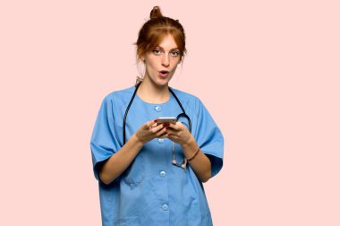 Genç redhead hemşire pembe arka plan üzerinde mobil ileti gönderme