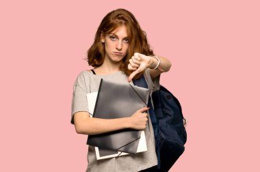 Başparmak işareti negatif ifade ile aşağı pembe arka plan üzerinde gösterilen genç redhead öğrenci