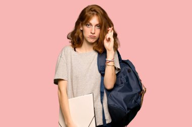 Pembe arka plan üzerinde en iyi dilek ve geçiş parmakları ile genç redhead öğrenci