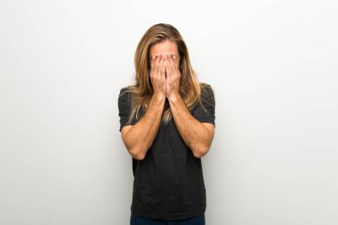 Yorgun ve hasta ifade ile beyaz duvarın üzerinden uzun saçlı sarışın adam