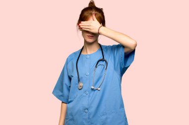 Gözleri eller tarafından kapsayan genç redhead hemşire. Bir şey pembe arka plan üzerinde görmek istiyor musunuz