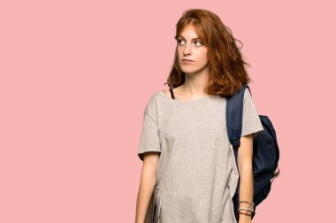 Pembe arka plan üzerinde ciddi bir yüz ile ararken genç redhead öğrenci