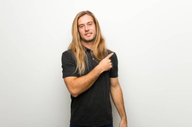 Beyaz duvar tarafına işaret üzerinde uzun saçlı sarışın adam bir ürün sunmak için