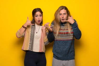 Hippi çift telefon jest yapma ve şüphe sarı arka plan üzerinde