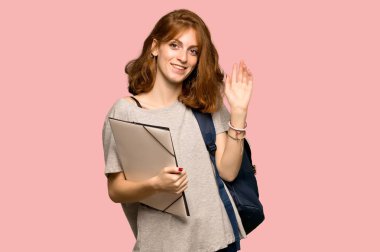 Pembe arka plan üzerinde el ile mutlu ifade ile selamlayan genç redhead öğrenci