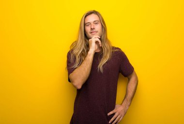 Gülümseyen ve öne doğru emin yüz ile seyir sarı duvarın üzerinden uzun saçlı sarışın adam