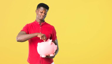 Sarı arka plan üzerinde dolu olduğu için kumbara ve mutlu çekici genç Afro-Amerikan adam