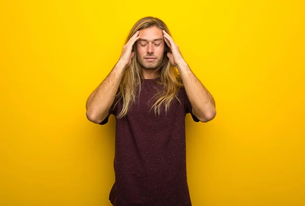 Blond man with long hair over yellow wall unhappy and frustrated with something