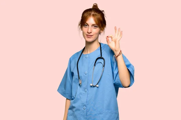 Молодая Рыжая Медсестра Показывает Знак Пальцами Розовом Фоне — стоковое фото
