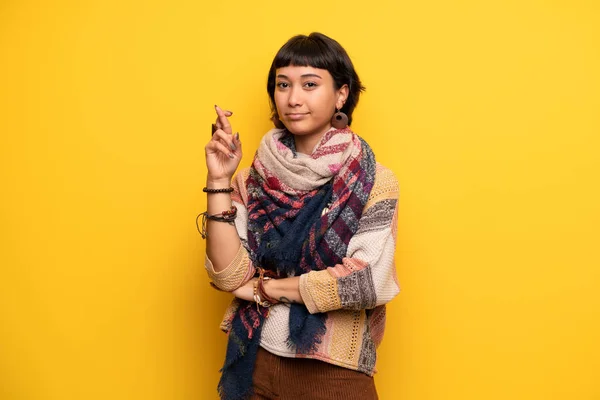 Young hippie woman over yellow wall with fingers crossing and wishing the best