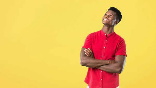 Young african american man stand and looking up while smiling on yellow background