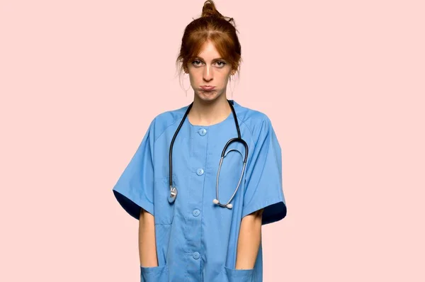 Jovem Enfermeira Ruiva Com Expressão Triste Deprimida Sobre Fundo Rosa — Fotografia de Stock
