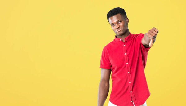 Young african american man showing thumb down sign with negative expression on yellow background