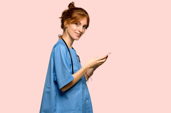 Young Redhead Nurse Sending Message Mobile Pink Background — Stock Photo, Image
