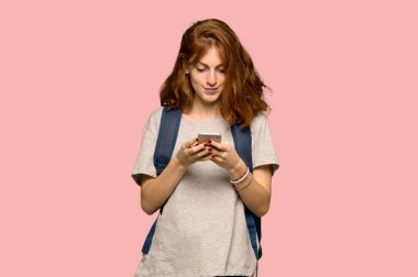 Genç redhead öğrenci pembe arka plan üzerinde mobil ileti gönderme