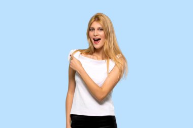 Parmak tarafına işaret ve izole mavi arka plan üzerinde bir ürün sunma sarışın genç kadın