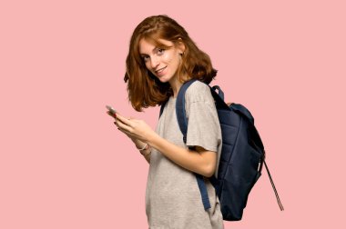 Genç redhead öğrenci pembe arka plan üzerinde mobil ileti gönderme