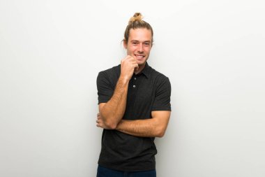 Tatlı bir ifadeyle gülümseyen beyaz duvarın üzerinden uzun saçlı sarışın adam