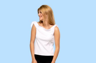 Genç sarışın kadın izole mavi arka plan üzerinde gülümseyen