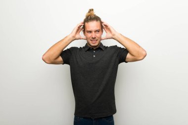 Beyaz duvar üzerinde uzun saçlı sarışın adam alır eller başının üstüne çünkü migren vardır