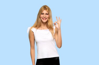 Sarışın genç kadın bir ok işareti parmak ile izole mavi arka plan üzerinde gösterilen