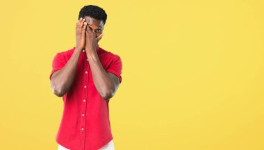 Gözleri eller tarafından kapsayan ve Sarı zemin üzerine parmaklarımın arasından arıyorum genç Afro-Amerikan adam