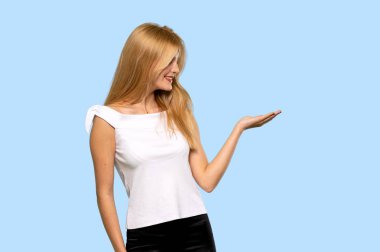 İzole mavi zemin üzerine bir reklam eklemek için boşaltmak hayali avuç içinde tutan genç sarışın kadın